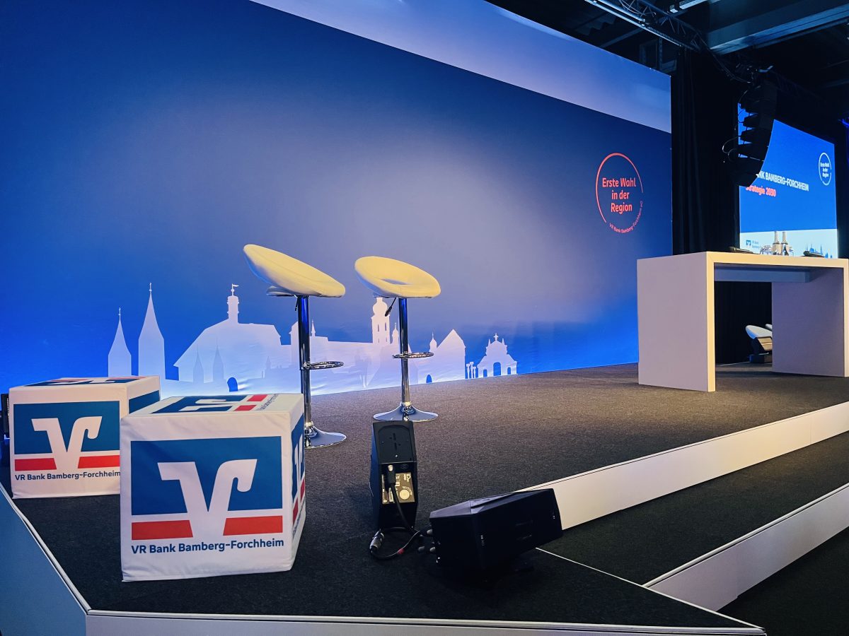 Inszenierte Bühne mit 36 m² großer, bespannter Bühnenrückwand im VR-Bank-Design in der element-e Halle im Energiepark Hirschaid – Licht- und Soundtechnik für den Jahresauftakt der VR Bank Bamberg-Forchheim.